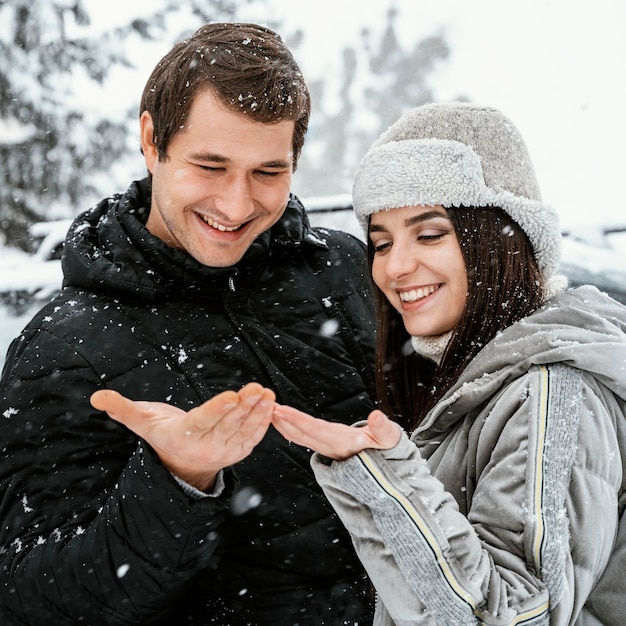 Vista frontal de la pareja sonriente disfrutando de la nieve durante un viaje por carretera