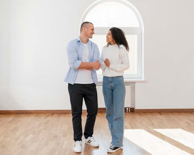 Vista frontal de la pareja sonriente en su nueva casa vacía