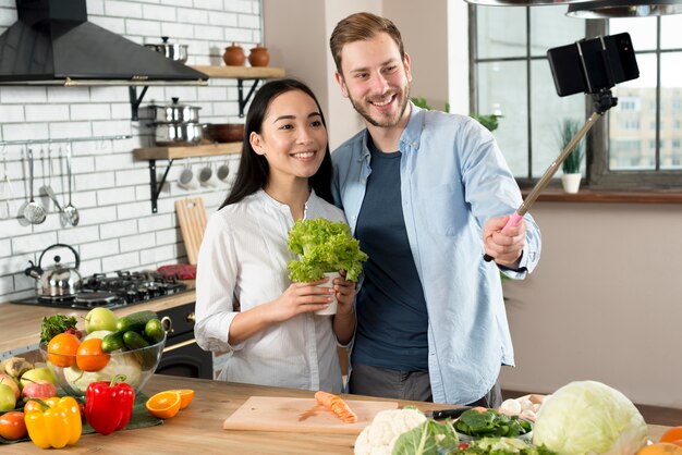 Vista frontal de la pareja sonriente tomando selfie en el teléfono móvil en la cocina