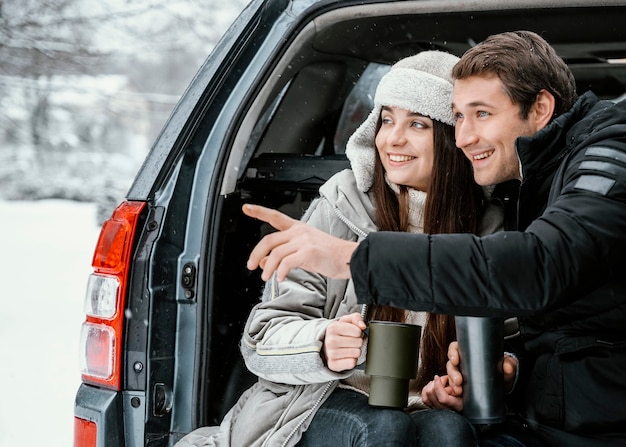 Foto gratuita vista frontal de la pareja tomando una bebida caliente en el maletero del coche durante un viaje por carretera