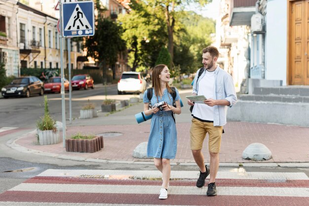 Vista frontal de la pareja de turistas con mapa y cámara en el cruce de peatones