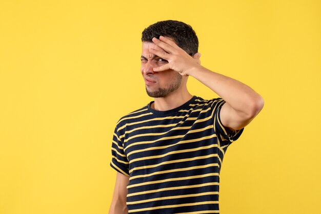 Vista frontal parpadeó -ojo joven en camiseta a rayas blanco y negro sobre fondo amarillo aislado