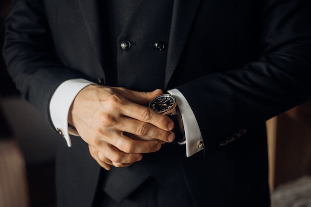 Vista frontal de la parte del pecho de un hombre vestido con un elegante traje negro y un precioso reloj, las manos del hombre