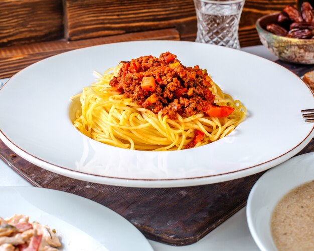 Vista frontal de pasta con carne dentro de un plato blanco en el piso marrón