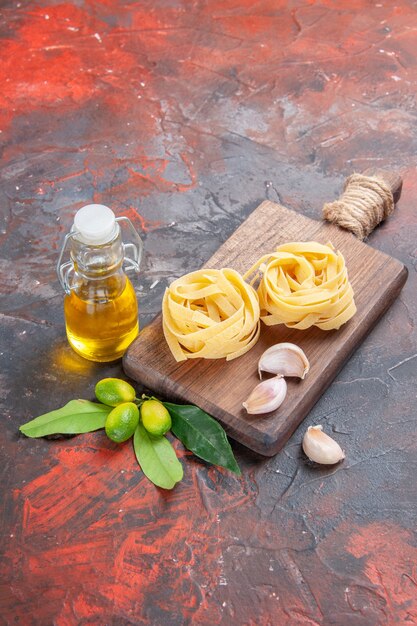 Vista frontal de la pasta cruda con aceite y ajo sobre la masa de pasta cruda de superficie oscura