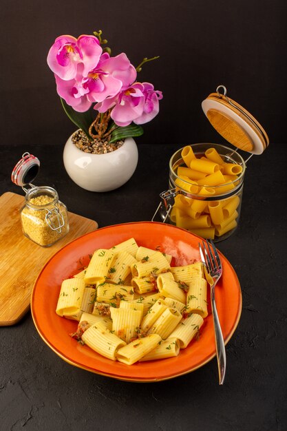 Una vista frontal de la pasta italiana cocida sabrosa salada dentro de la placa redonda de naranja con flores dentro de la inmersión en la alfombra diseñada y escritorio oscuro