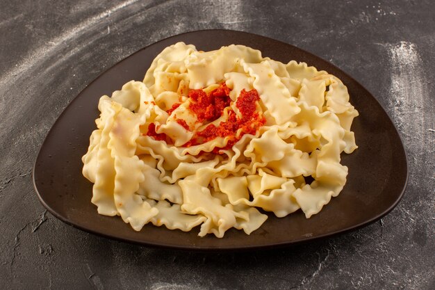 Una vista frontal de pasta italiana cocida con salsa de tomate dentro de la placa sobre la superficie gris