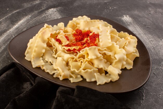 Una vista frontal de pasta italiana cocida con salsa de tomate dentro de la placa sobre la superficie gris