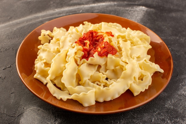 Una vista frontal de pasta italiana cocida con salsa de tomate dentro de la placa sobre la superficie gris