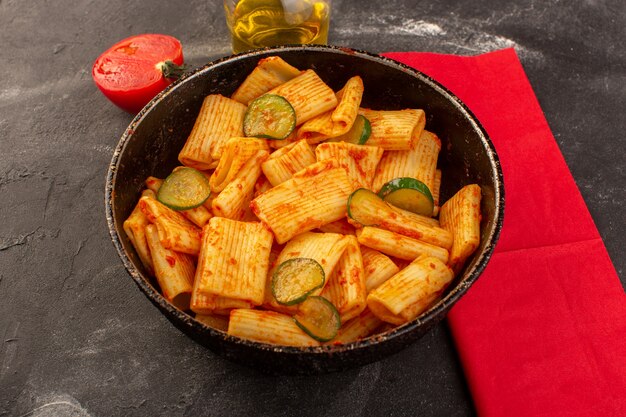 Una vista frontal de pasta italiana cocida con salsa de tomate y pepino dentro de la cacerola en el escritorio oscuro