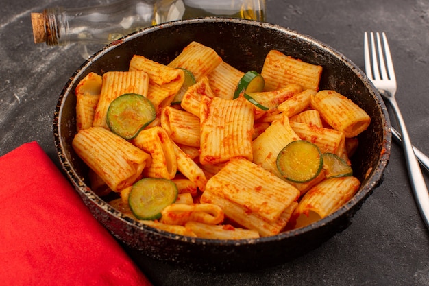 Una vista frontal de pasta italiana cocida con salsa de tomate y pepino dentro de la sartén sobre la superficie oscura