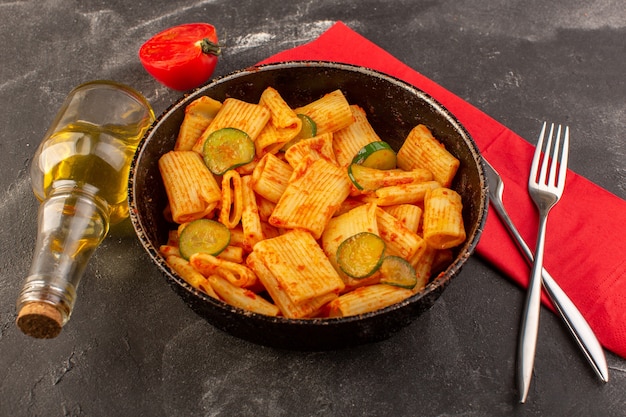 Una vista frontal de pasta italiana cocida con salsa de tomate y pepino dentro de la sartén sobre la superficie oscura