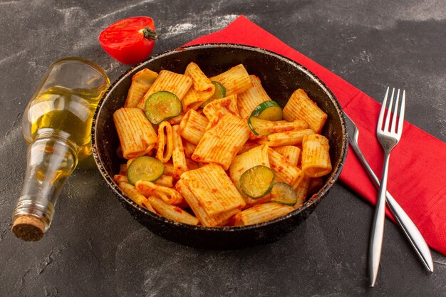 Una vista frontal de pasta italiana cocida con salsa de tomate y pepino dentro de la sartén sobre la superficie oscura