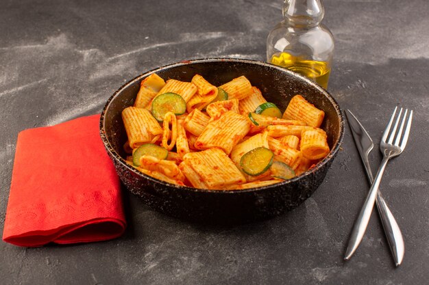 Foto gratuita una vista frontal de pasta italiana cocida con salsa de tomate y pepino dentro de la sartén sobre la superficie oscura