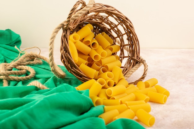 Una vista frontal de pasta italiana cruda amarilla dentro de la canasta junto con cuerdas en tejido verde