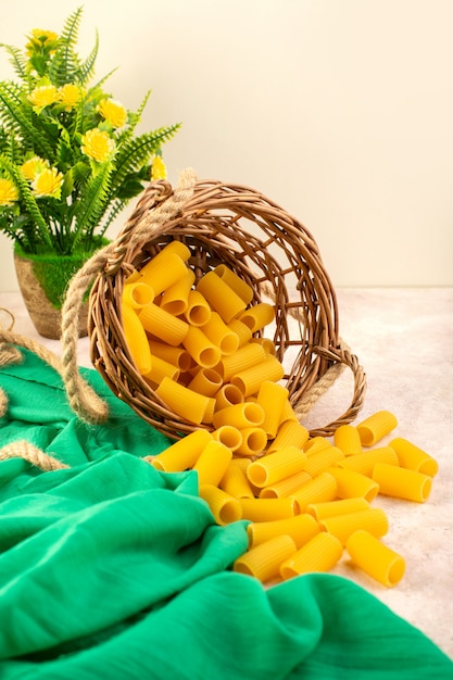 Una vista frontal de pasta italiana cruda amarilla dentro de la canasta junto con cuerdas en tejido verde