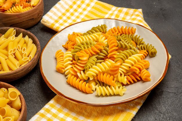 Vista frontal de la pasta italiana cruda diferentes formados dentro de las placas en el escritorio gris cocinar pasta italiana cruda