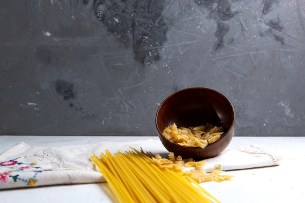 Foto gratuita una vista frontal de pasta italiana cruda largo y pequeño tazón de pasta