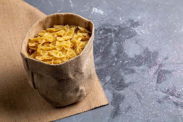 Una vista frontal de la pasta italiana cruda poco formada dentro de la bolsa en la mesa gris comida italiana