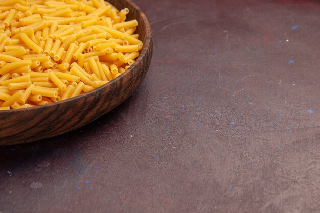 Vista frontal de la pasta italiana cruda poco formada dentro de la placa en el escritorio oscuro