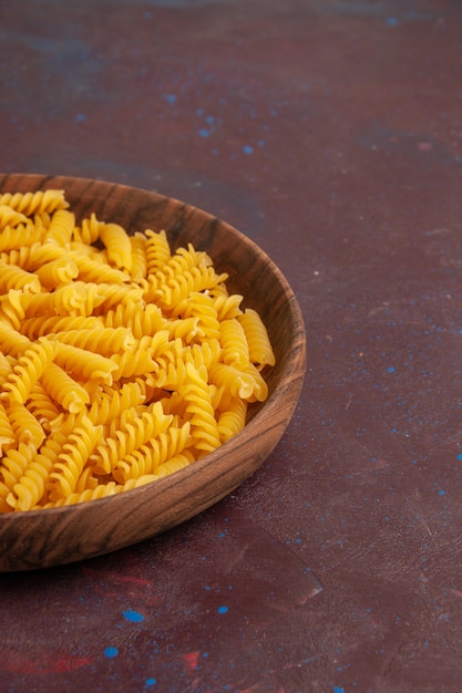 Vista frontal de la pasta italiana cruda poco formada dentro de la placa en el escritorio oscuro