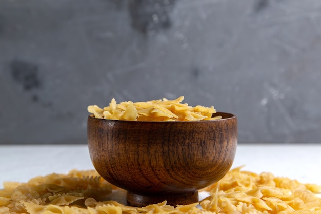 Una vista frontal de pasta italiana cruda poco formado dentro de la placa marrón en la mesa brillante comida italiana de pasta