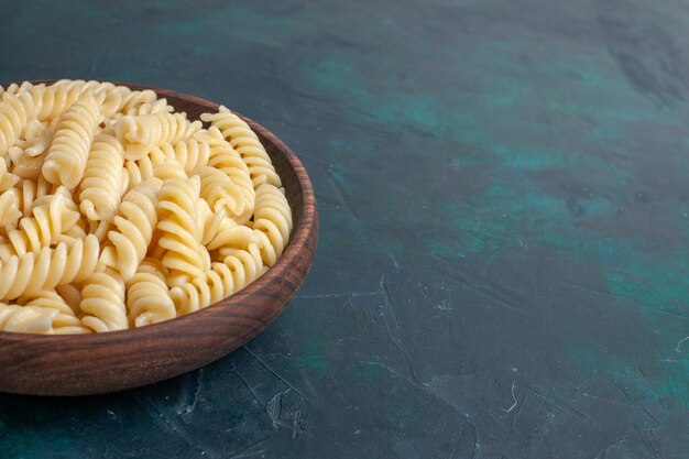Vista frontal de la pasta italiana en forma de delicioso aspecto poco de pasta dentro de una olla marrón en el escritorio azul oscuro