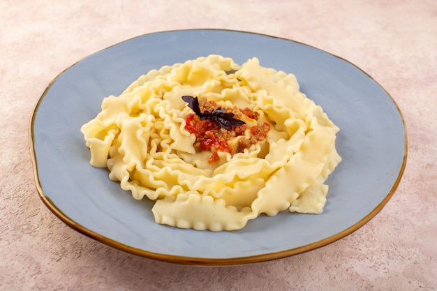 Una vista frontal de la pasta de masa cocida sabrosa y salada con carne y verduras dentro de la placa azul redonda en el escritorio rosa