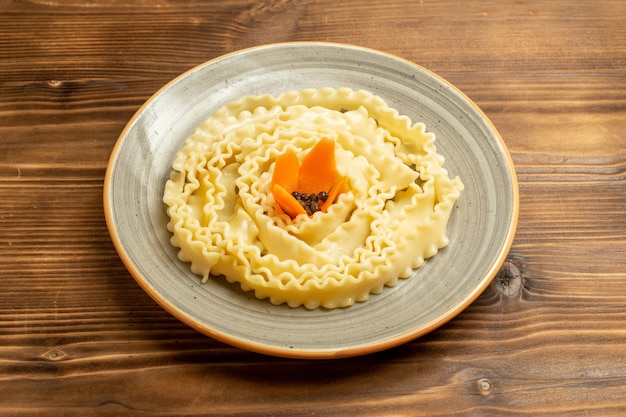 Vista frontal de la pasta de masa cruda formada dentro de la placa en la mesa marrón pasta de comida cruda de masa