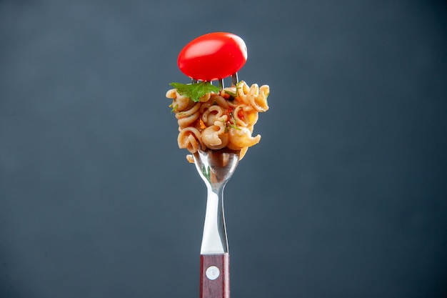 Vista frontal de pasta rotini con tomate cherry en horquilla sobre superficie gris aislada con espacio libre