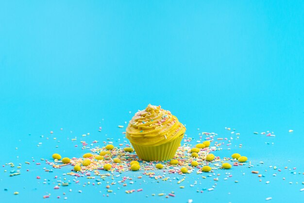 Vista frontal de un pastel amarillo con pequeñas partículas de caramelo de colores en el escritorio azul, pastel de galleta dulce