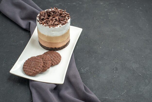 Vista frontal de pastel de chocolate y galletas en placa rectangular blanca mantón morado en lugar libre oscuro