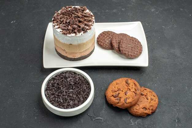 Vista frontal de pastel de chocolate y galletas en un tazón de plato rectangular blanco con galletas de chocolate negro sobre fondo oscuro aislado