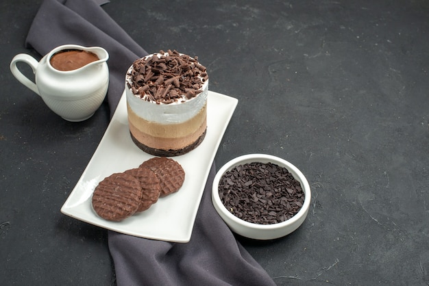 Vista frontal de pastel de chocolate y galletas en tazones de fuente rectangular blanca con chal de chocolate púrpura sobre fondo oscuro aislado espacio libre