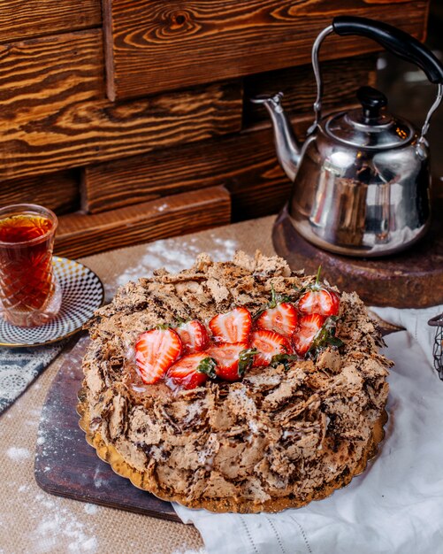 Vista frontal pastel de chocolate marrón con strawerries rojos frescos en la parte superior junto con té caliente en el piso marrón