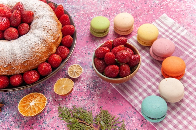 Vista frontal de pastel de fresa pastel de azúcar en polvo con macarons en rosa