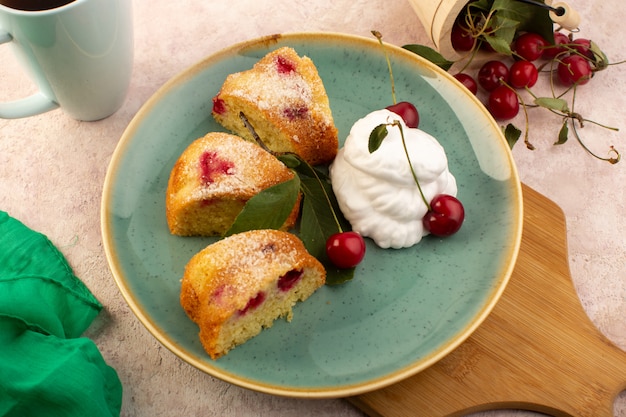 Una vista frontal pastel de frutas horneado delicioso en rodajas con cerezas rojas en el interior y azúcar en polvo dentro de la placa redonda verde con té en rosa