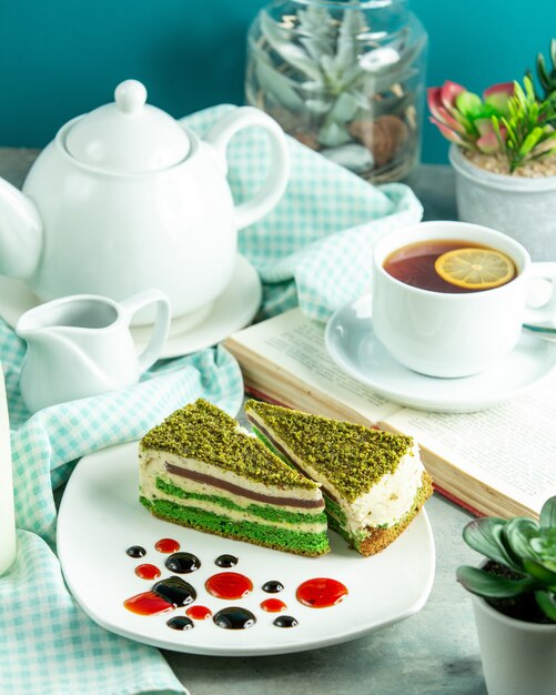 Vista frontal de pastel de pistacho con una taza de té y una rodaja de limón