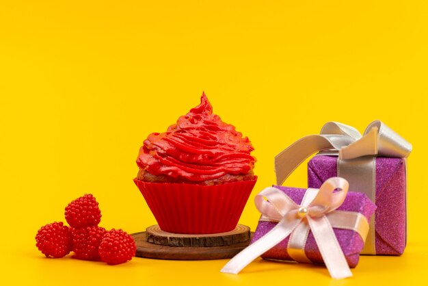 Vista frontal de un pastel rojo con frambuesas rojas frescas y cajas de regalo de color púrpura en el escritorio amarillo