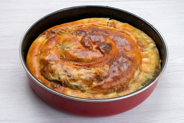 Vista frontal del pastel de verduras cocidas dentro de una sartén redonda sobre la superficie blanca