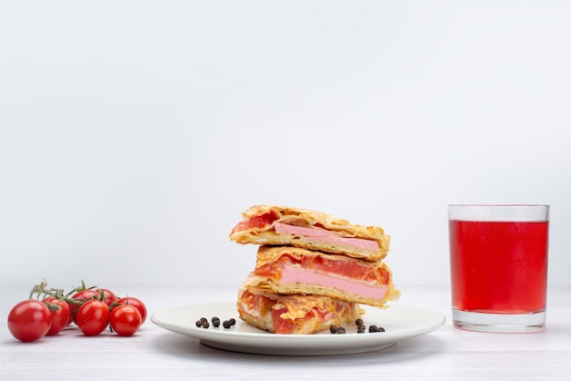 Vista frontal de pastelería vegetal en rodajas dentro de la placa blanca junto con tomates y jugo en blanco ¡