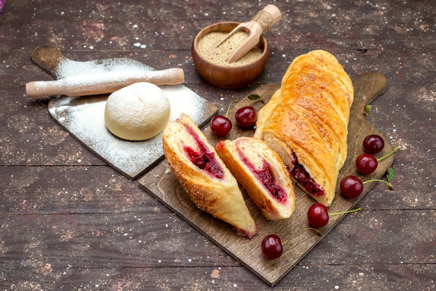 Vista frontal de pasteles de cerezas deliciosas y dulces con guindas frescas en el escritorio de madera marrón