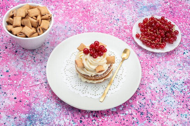 Vista frontal de pasteles con crema junto con arándanos y galletas en el escritorio de color