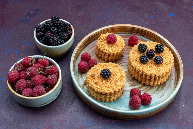 Vista frontal de pasteles dulces y deliciosos con bayas frescas sobre superficie oscura