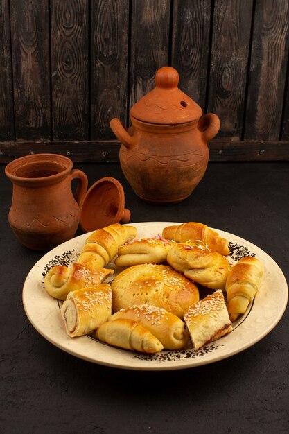 Vista frontal pasteles marrones dulces cocinados dentro de un plato blanco en la oscuridad