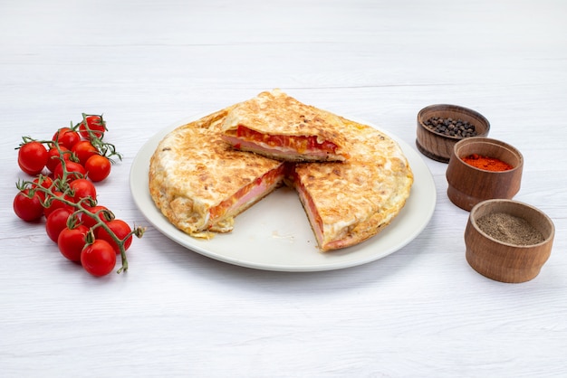 Vista frontal de pasteles de verduras cocidas dentro de un plato blanco con tomates rojos frescos en la superficie blanca