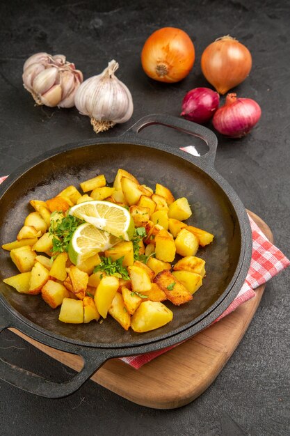 Vista frontal de las patatas fritas dentro de la sartén con limón y verduras en la mesa oscura