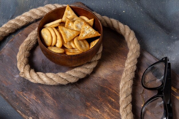 Vista frontal de patatas fritas y galletas con cuerdas y gafas de sol en la superficie gris