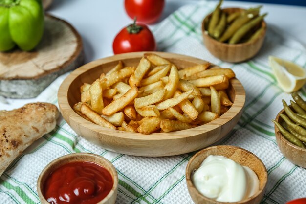 Vista frontal de patatas fritas con salsa de tomate y mayonesa, tomates y pimientos sobre la mesa