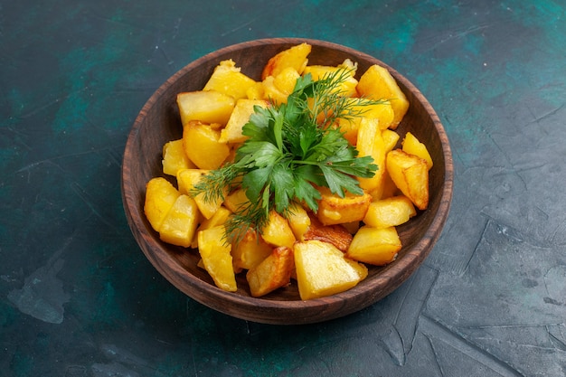 Vista frontal de patatas en rodajas cocidas con verduras dentro de la placa marrón sobre una superficie azul oscuro